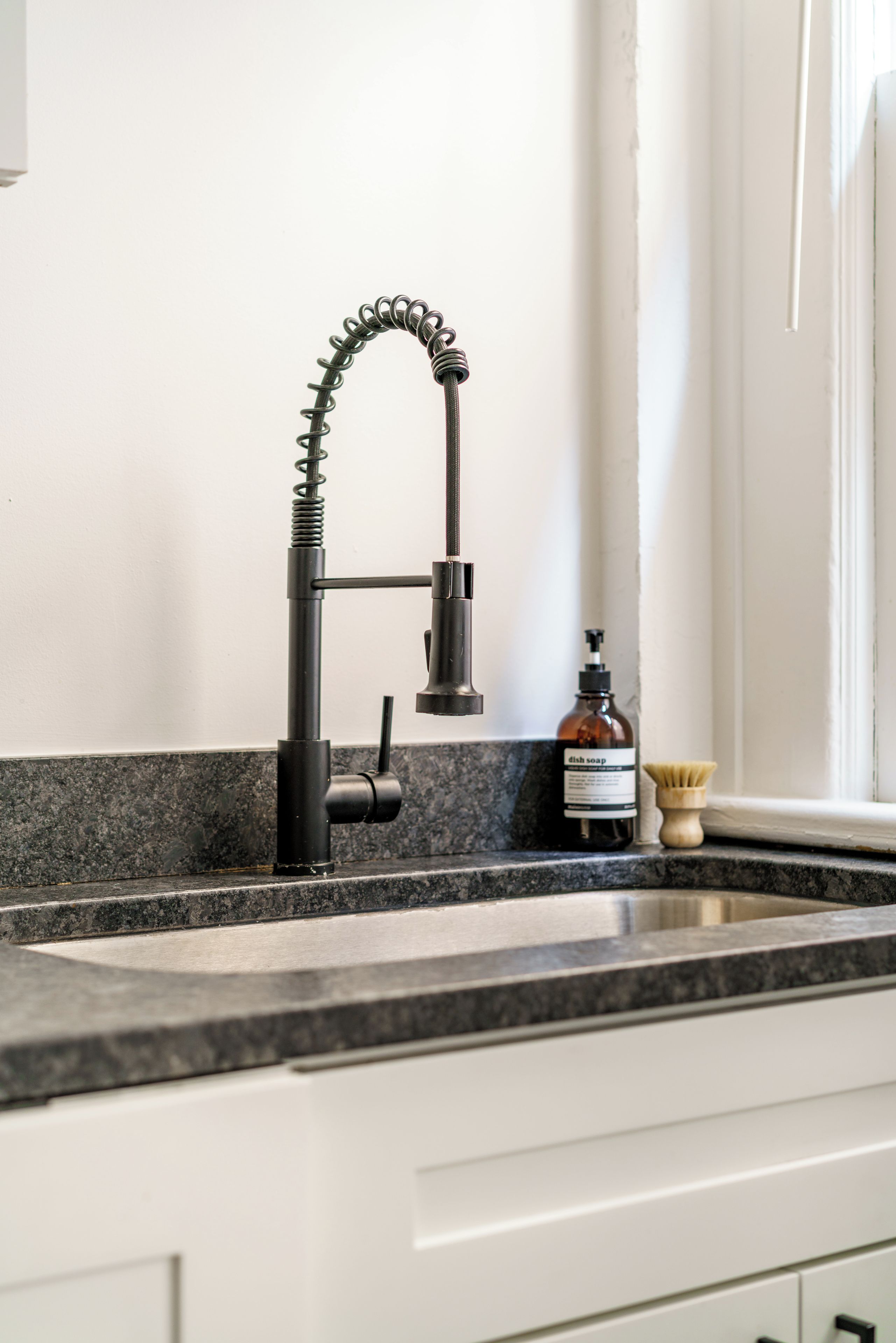A kitchen with a modern faucet, a soap dispenser, and a brush on the counter.