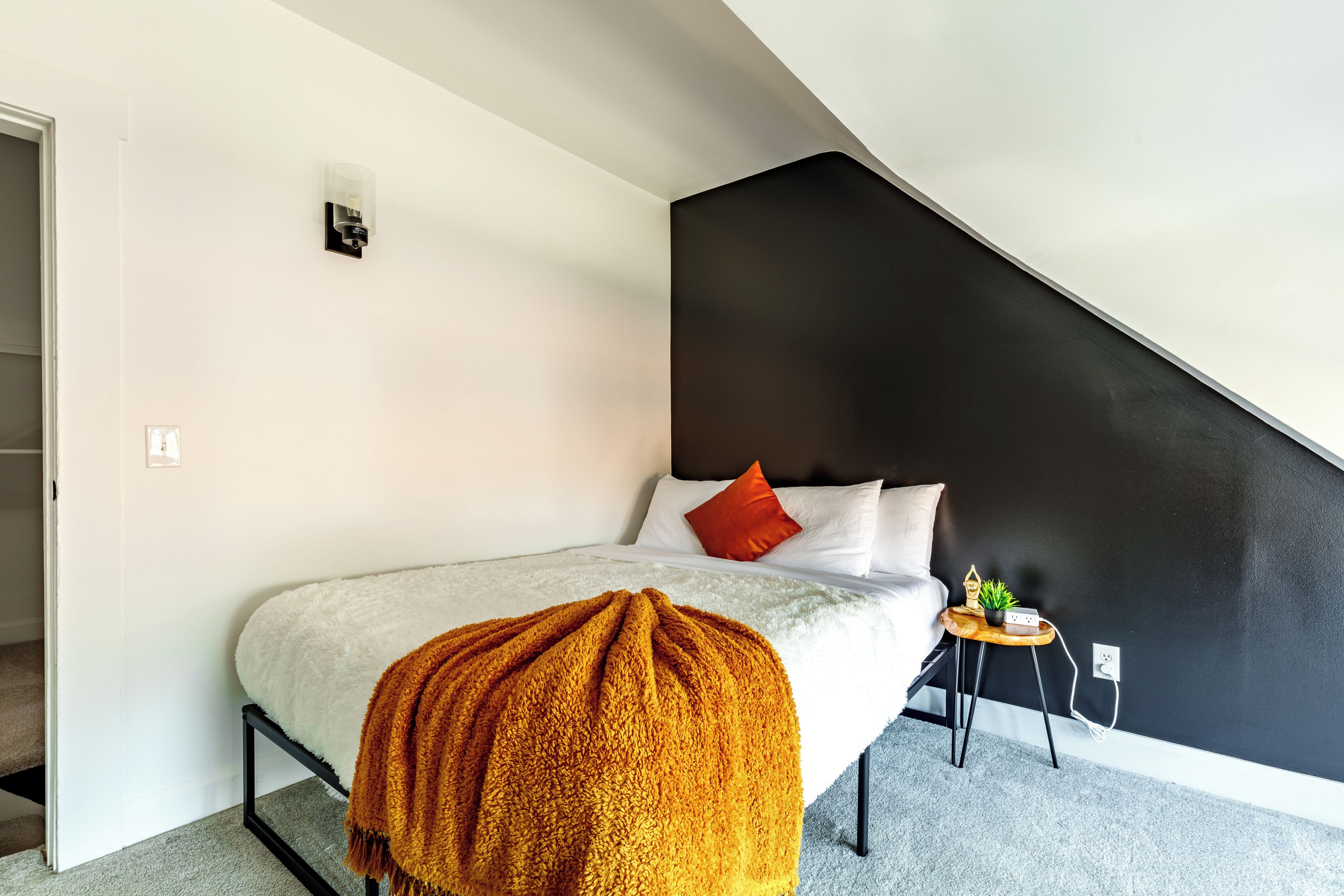 A bedroom with a bed, a small side table, a wall-mounted light, and a staircase.