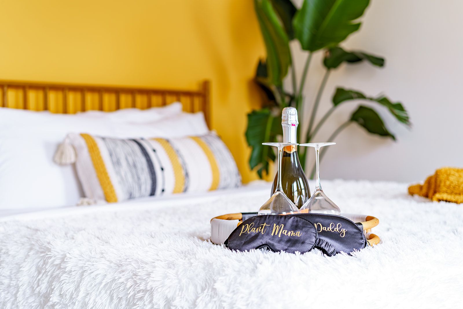 A bed with a white fluffy blanket, a bedside table with a bottle and glasses, and a pillow with a yellow and white striped pillowcase.