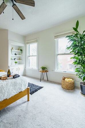 A bedroom with a bed, a wooden ceiling fan, a white fluffy rug, a small wooden table with a plant, and a large potted plant. - Jungle House Boutique Residences – Downtown Columbus & Short North (Columbus)