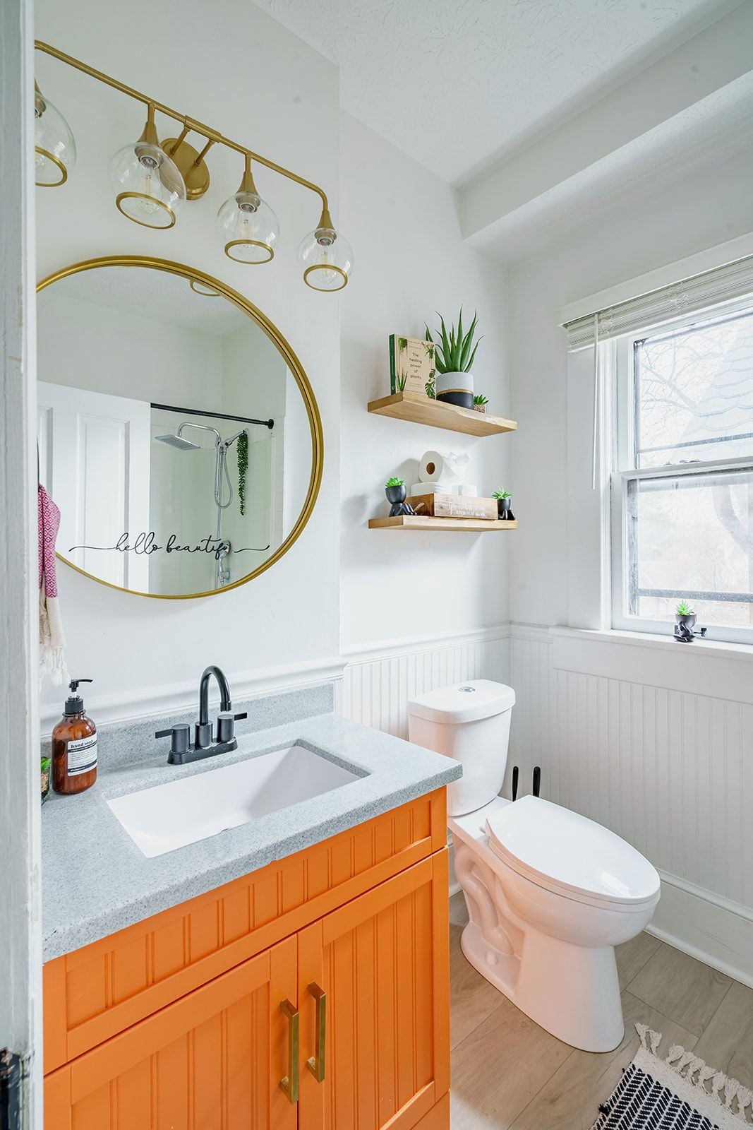 A bathroom with a white sink, a white toilet, a gold-framed mirror, and a window with a view.