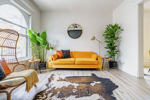 Un salon moderne avec un canapé, un miroir rond, une plante en pot, une lampe sur pied et un tapis en peau de vache.