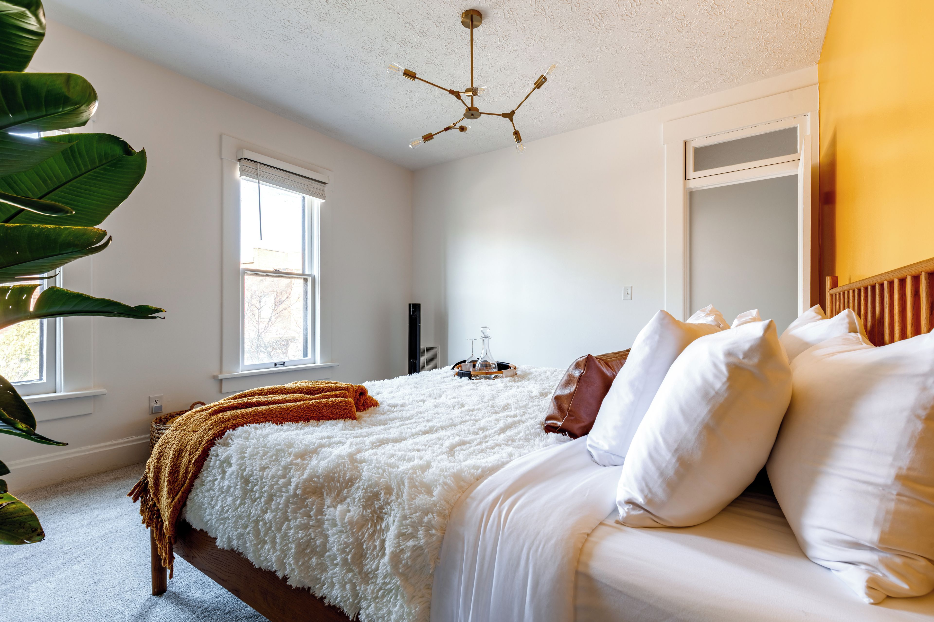 A bedroom with a bed, white bedding, a brown throw blanket, a ceiling fan, and a window.