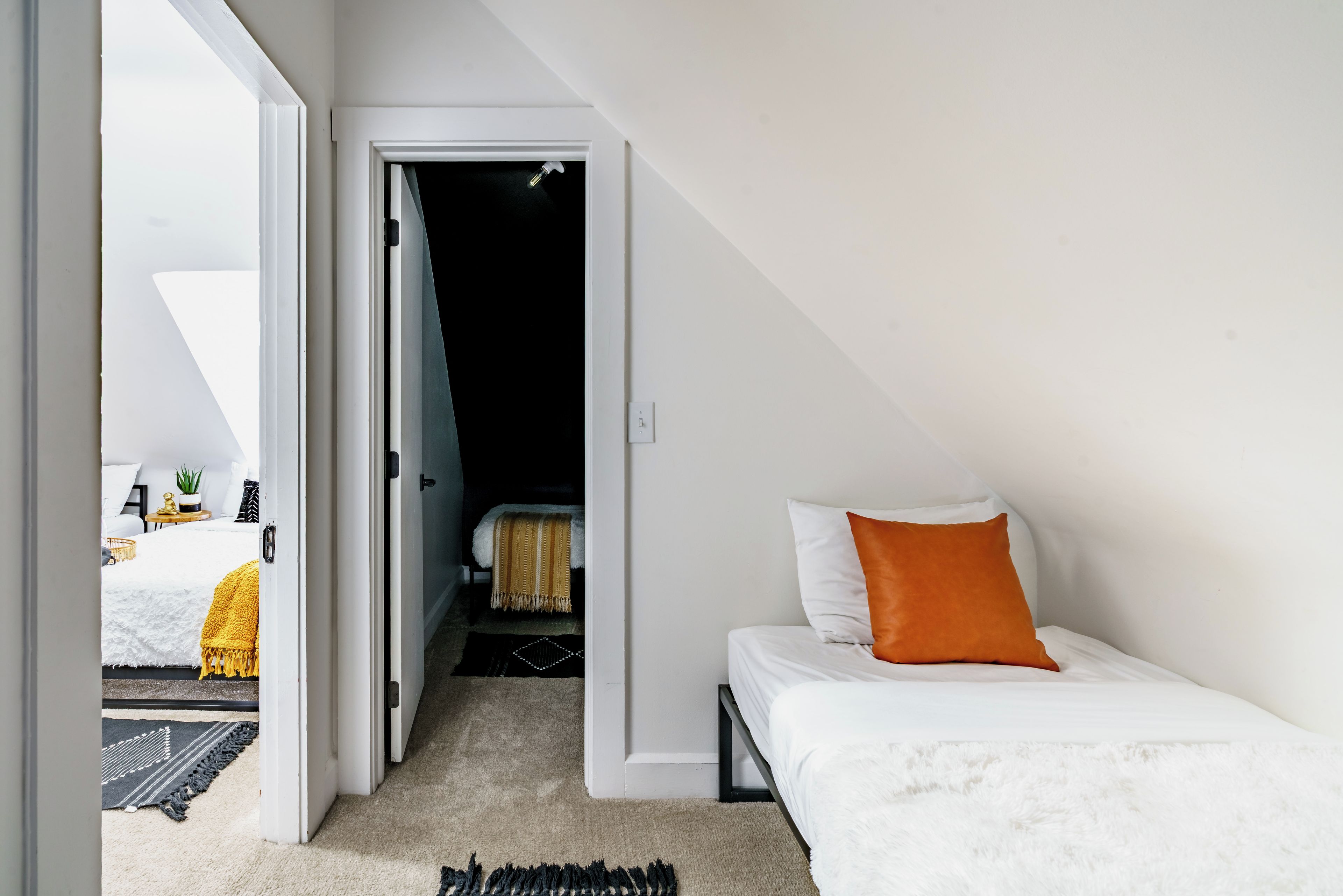 Un dormitorio con cama, mesita de noche, lámpara y vista a otra habitación.