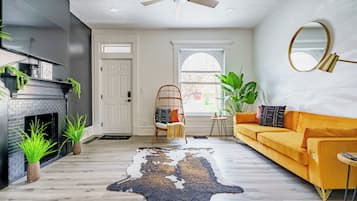 A living room with a sofa, a chair, a fireplace, a ceiling fan, and a large window.
