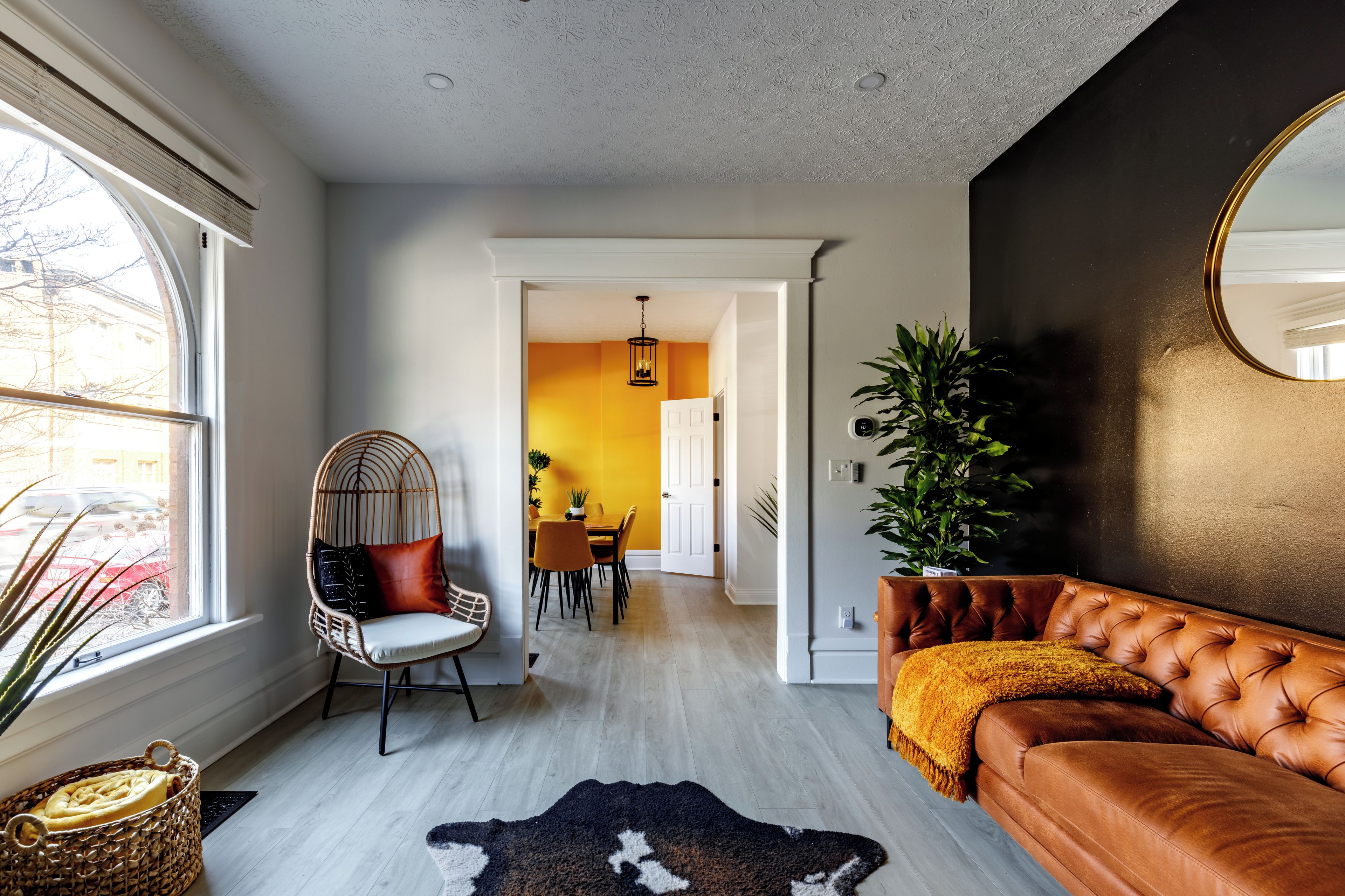 Ein modernes Wohnzimmer mit Ledersofa, einem gewebten Sessel, einem Kuhfellteppich und einem großen Spiegel.