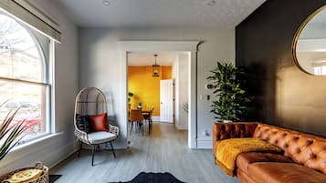 A modern living room with a leather sofa, a woven chair, a cowhide rug, and a large mirror.