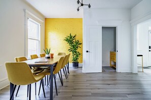 A dining area with a wooden table and chairs, a potted plant, and a yellow brick wall. - Jungle House Boutique Residences – Downtown Columbus & Short North (Columbus)