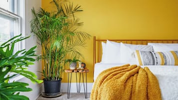 Une chambre à coucher avec un lit, un mur jaune, une fenêtre et une plante en pot.