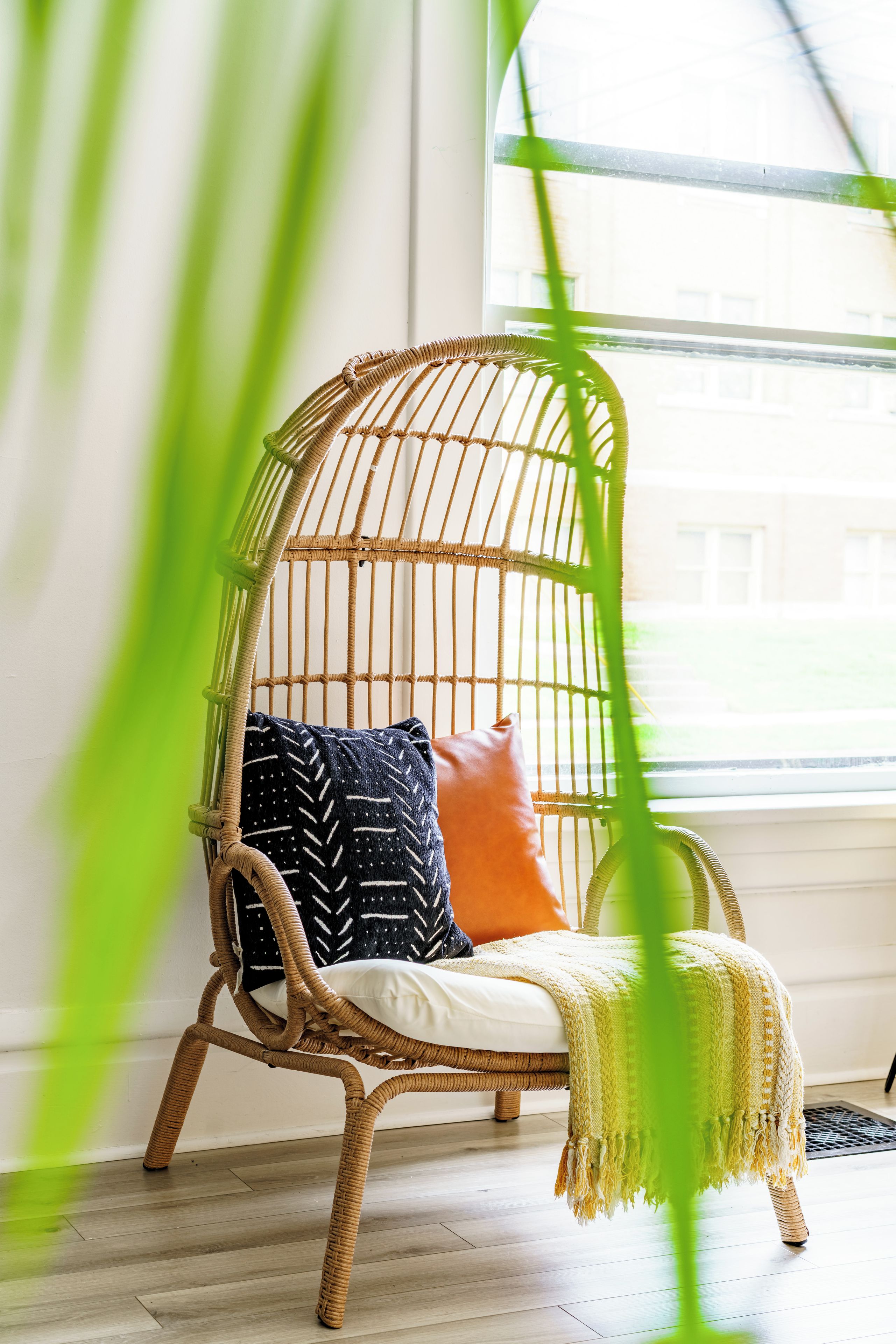 Une chaise en osier avec des coussins, dans une pièce dont le sol est en bois et qui possède une fenêtre.