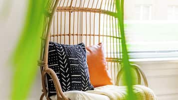 Une chaise en osier avec des coussins, dans une pièce dont le sol est en bois et qui possède une fenêtre.