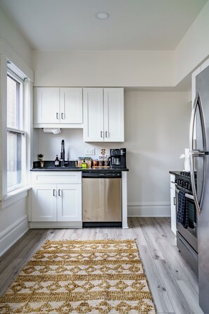 A modern kitchen with white cabinets, a stainless steel dishwasher, and a built-in oven. - Jungle House Boutique Residences – Downtown Columbus & Short North (Columbus)