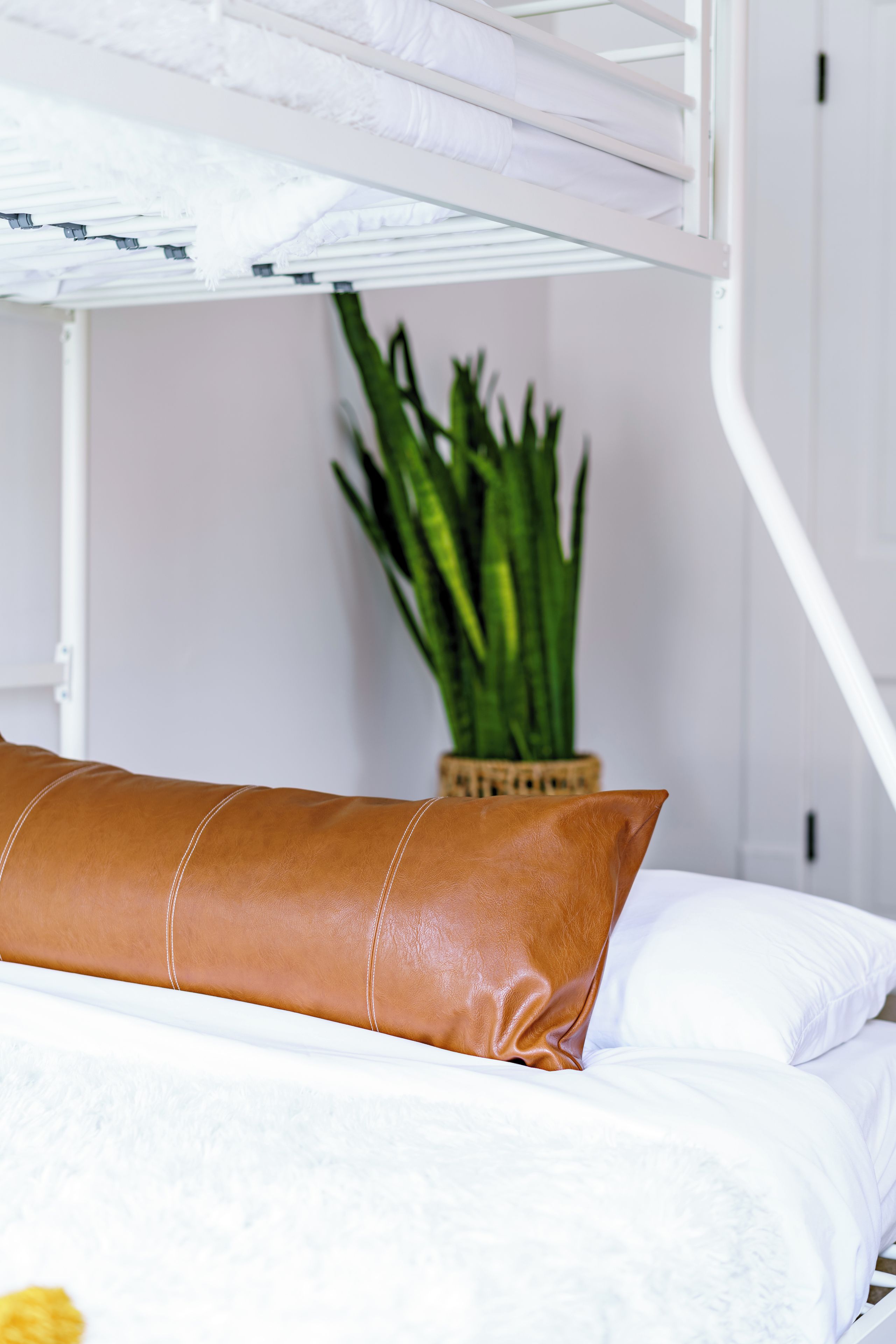A bunk bed with white bedding and a brown pillow.