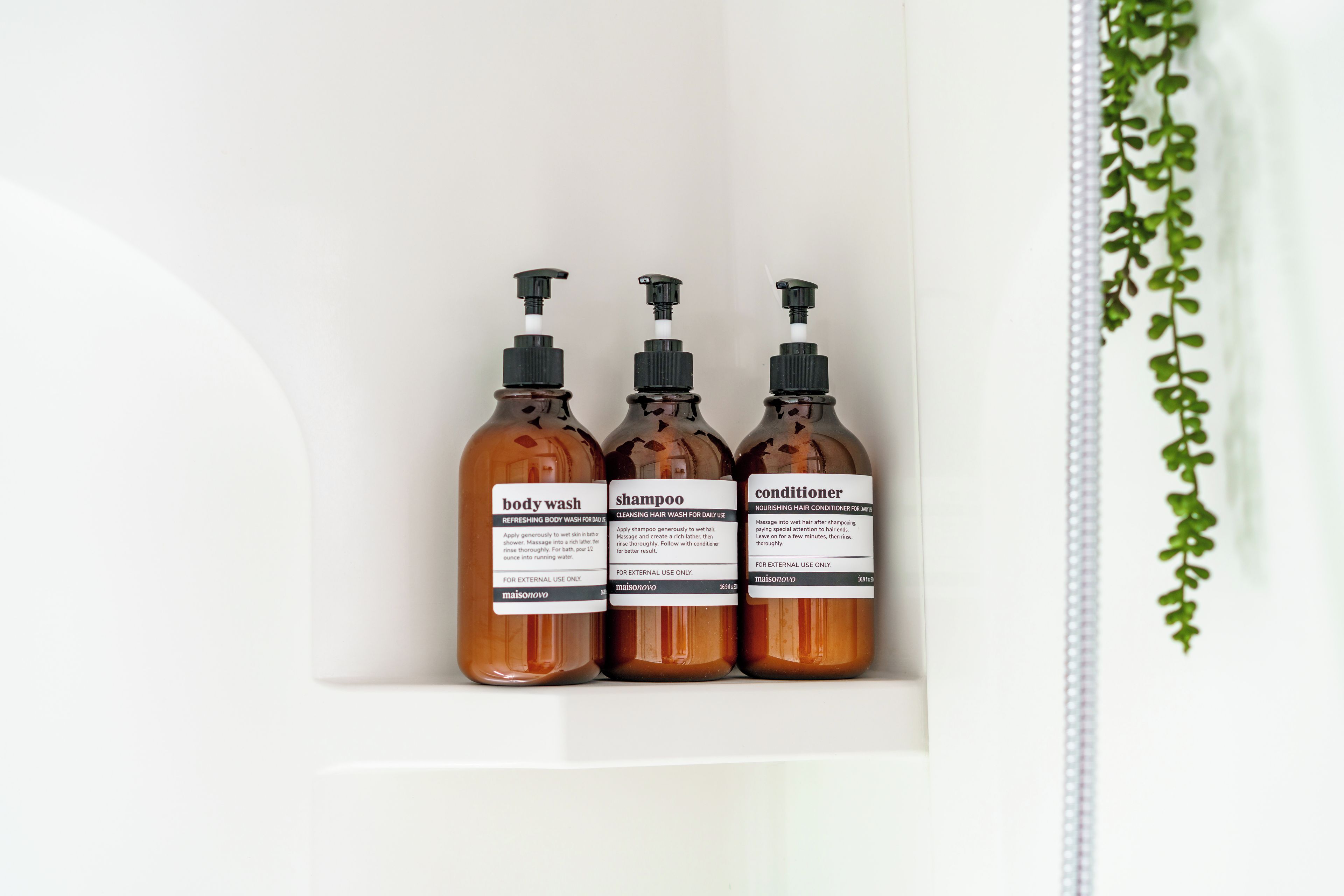 Three bottles of body wash, shampoo, and conditioner in a white shelf.