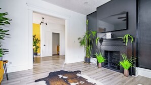 A modern living room with a fireplace, wooden flooring, and several potted plants.