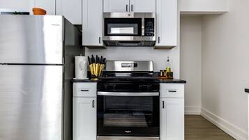 Una cocina moderna con electrodomésticos de acero inoxidable, armarios blancos y piso de madera.