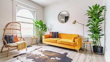 Un salon avec un canapé, un fauteuil, un grand miroir et des plantes en pot.