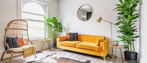 A living room with a sofa, a chair, a large mirror, and potted plants.