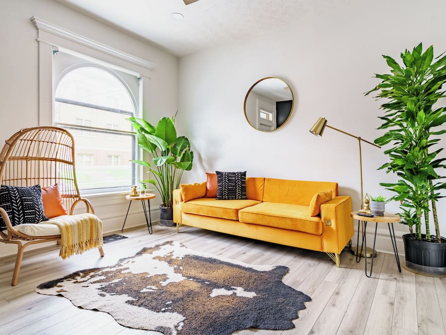 A living room with a sofa, a chair, a large mirror, and potted plants.
