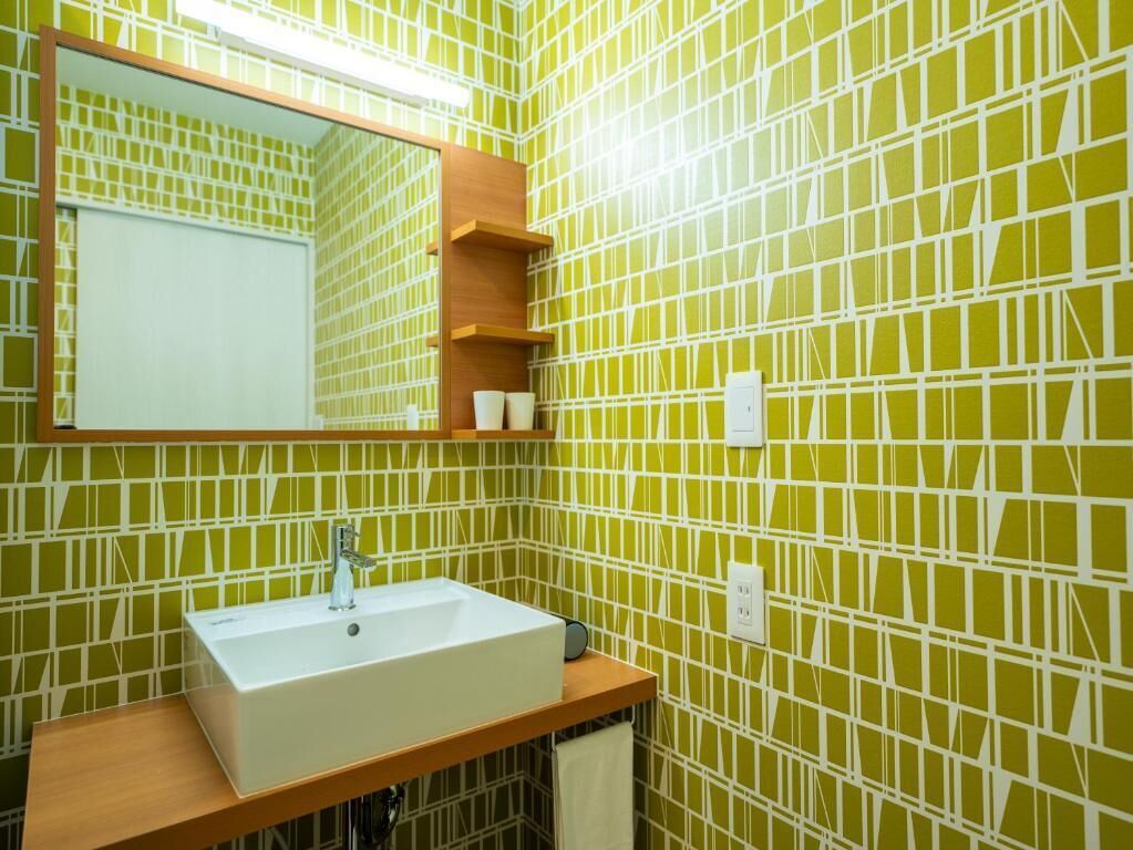Une salle de bain avec un lavabo blanc, un miroir et un mur recouvert de carreaux verts.