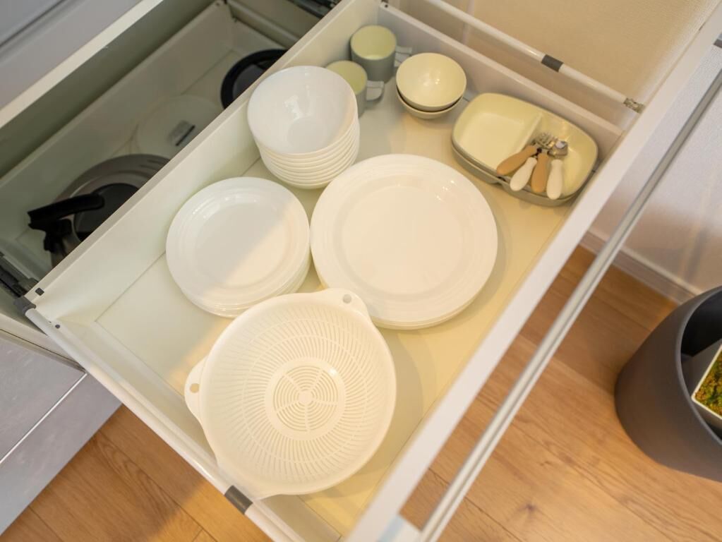 A kitchen drawer with white plates, bowls, and a colander.