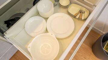 A kitchen drawer with white plates, bowls, and a colander.