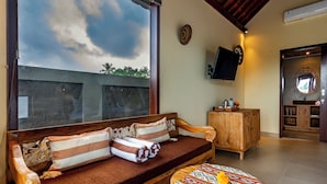 A cozy room with a wooden sofa, a small round table, and a television mounted on the wall. - Shankara Villa Ubud by Dhananjaya Hospitality (Sebatu)
