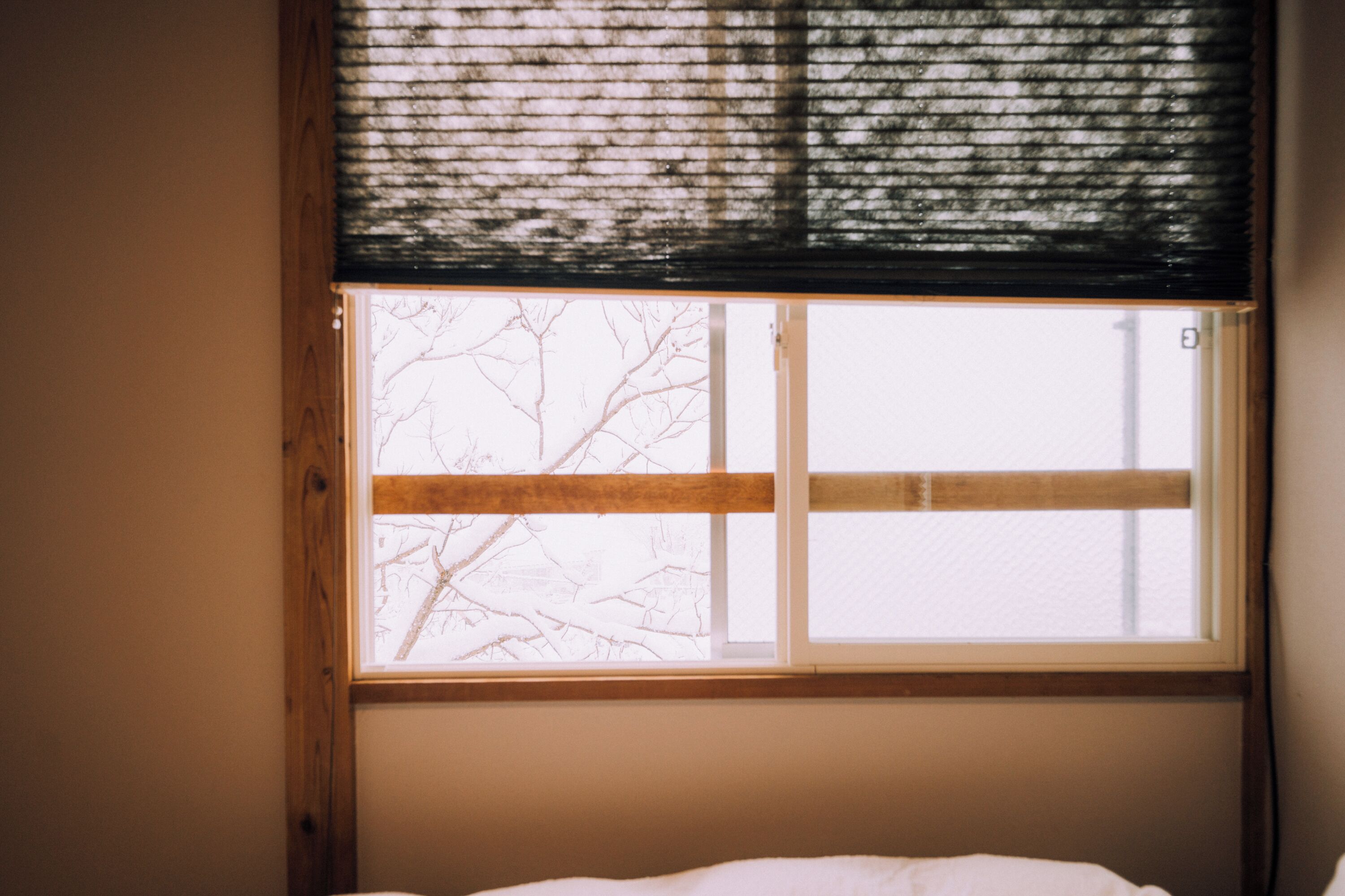 A window with a view of bare tree branches outside, a wooden frame, and a white window blind.