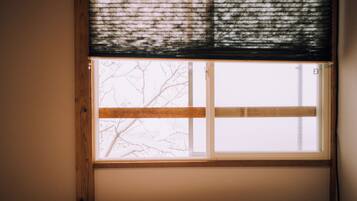 A window with a view of bare tree branches outside, a wooden frame, and a white window blind.