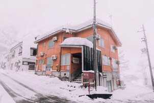 Un edificio con facciata rossa, una scalinata che conduce all'ingresso e un segnale che indica un'area di parcheggio.