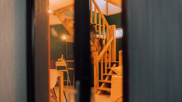 A wooden staircase with a plant on the railing, a dining area with chairs and a table, and a view of the interior space. - 3BD Yuzawa Onsen Lodge - House B (Minamiuonuma)