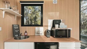 Eine kompakte Küche mit Fenster, einer Mikrowelle, einer Kaffeemaschine und einem Spülbecken.