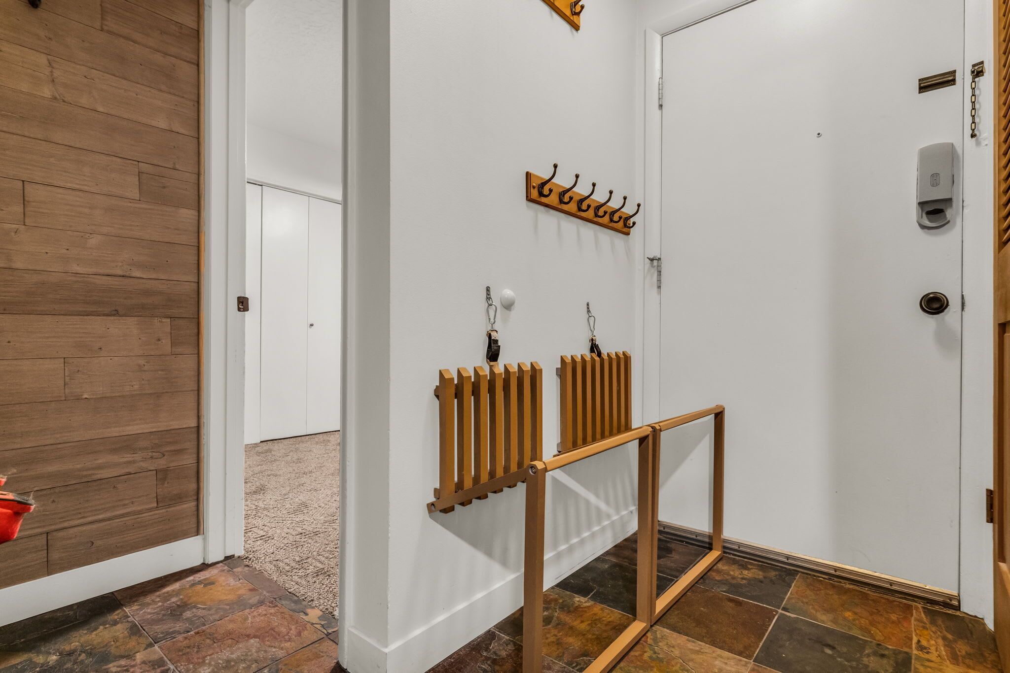 Un couloir avec un plancher en bois, une porte blanche, un porte-manteau et un radiateur.