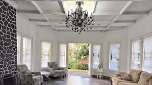 A spacious living room with a stone wall, a chandelier, and a large beige sofa. - Villa Narendra Yogyakarta (Pakem)