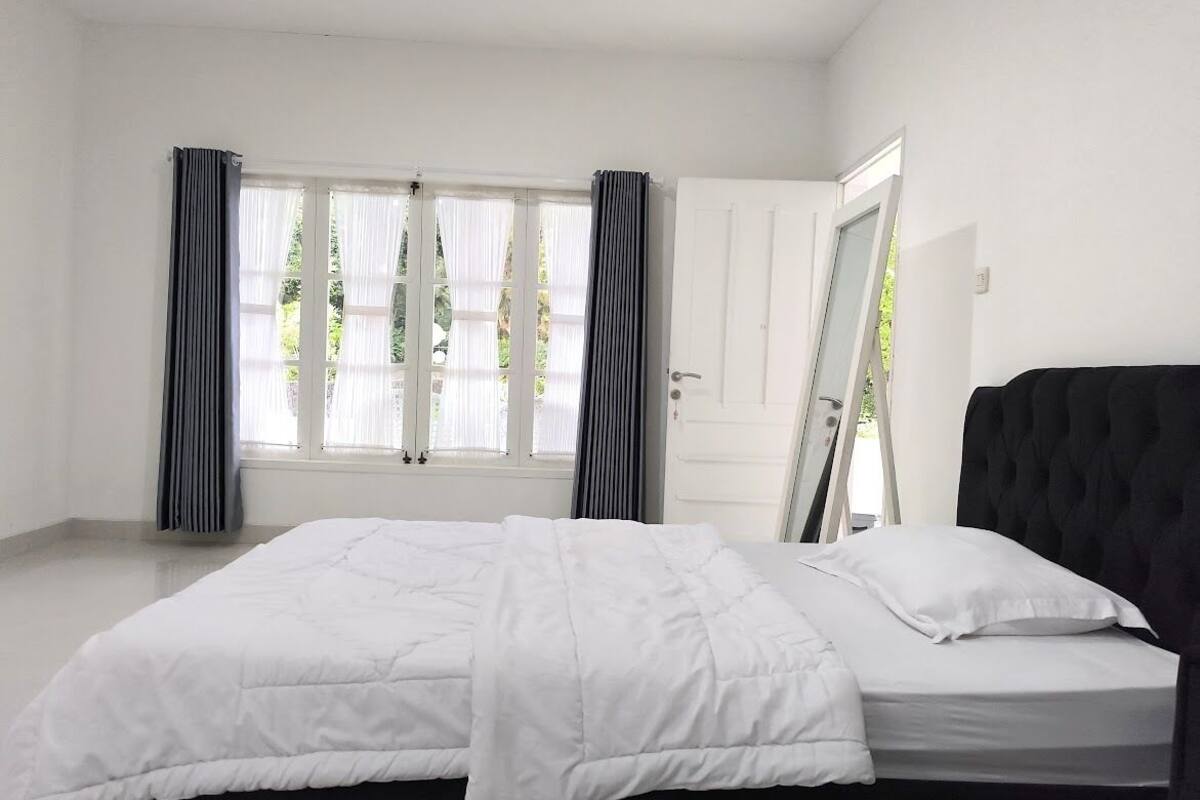 A bedroom with a large bed, white walls, and a window with curtains.
