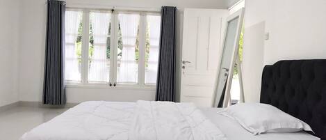 A bedroom with a large bed, white walls, and a window with curtains.
