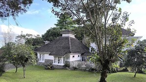 A house with a white exterior and dark roof, surrounded by a well-maintained lawn and trees. - Villa Narendra Yogyakarta (Pakem)