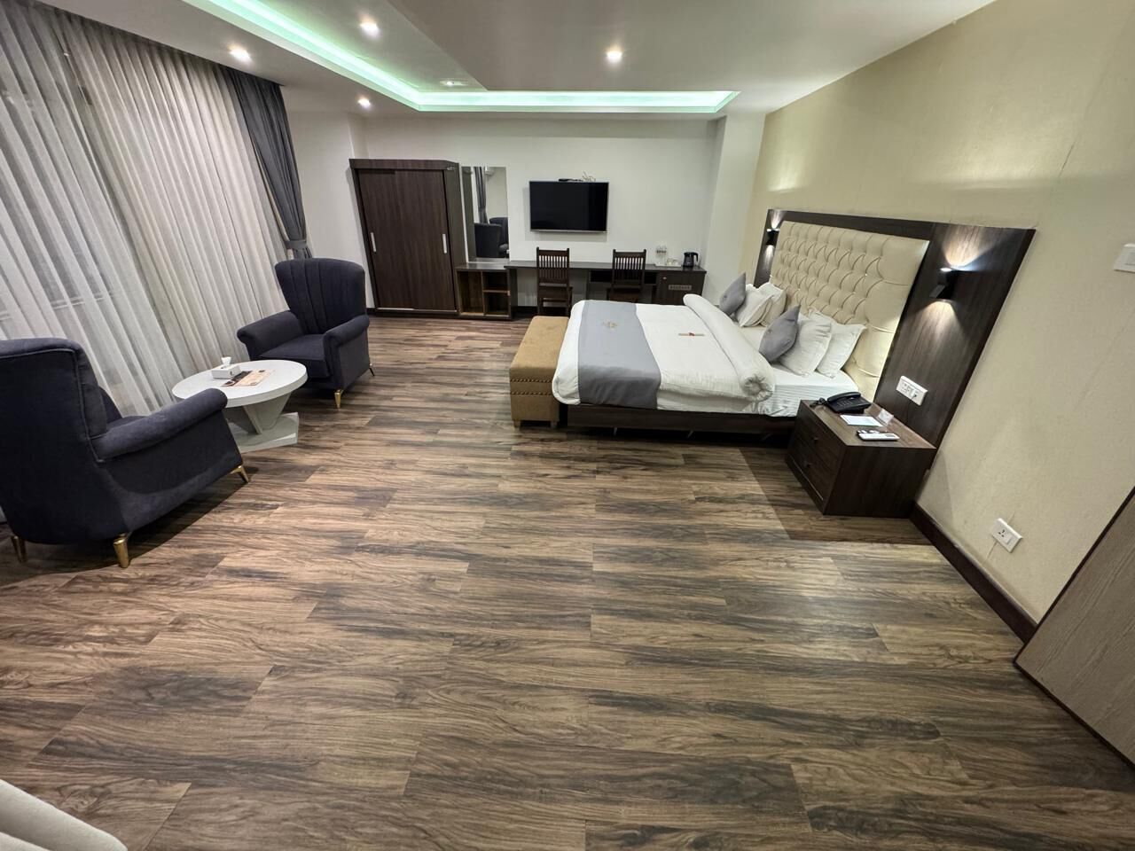 A modern hotel room with a large bed, a desk, a chair, and a TV.
