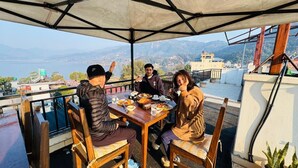 A group of people dining at an outdoor table with a view of mountains and a body of water. - Maharaja The Royal Hotel (Pokhara)