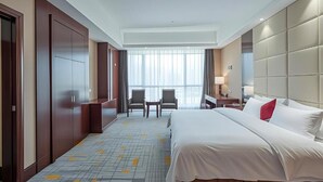 Una habitación de hotel con una cama grande, dos sillas, una mesita y una ventana con cortinas.