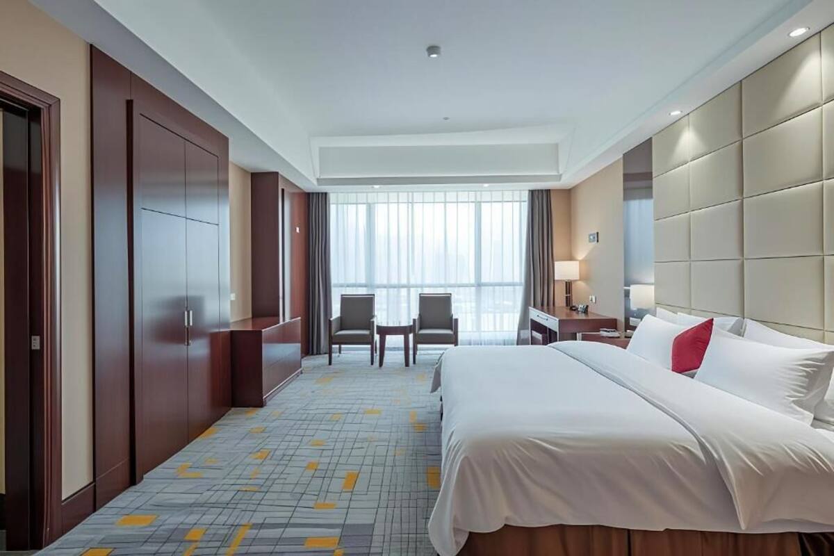 Una habitación de hotel con una cama grande, dos sillas, una mesita y una ventana con cortinas.