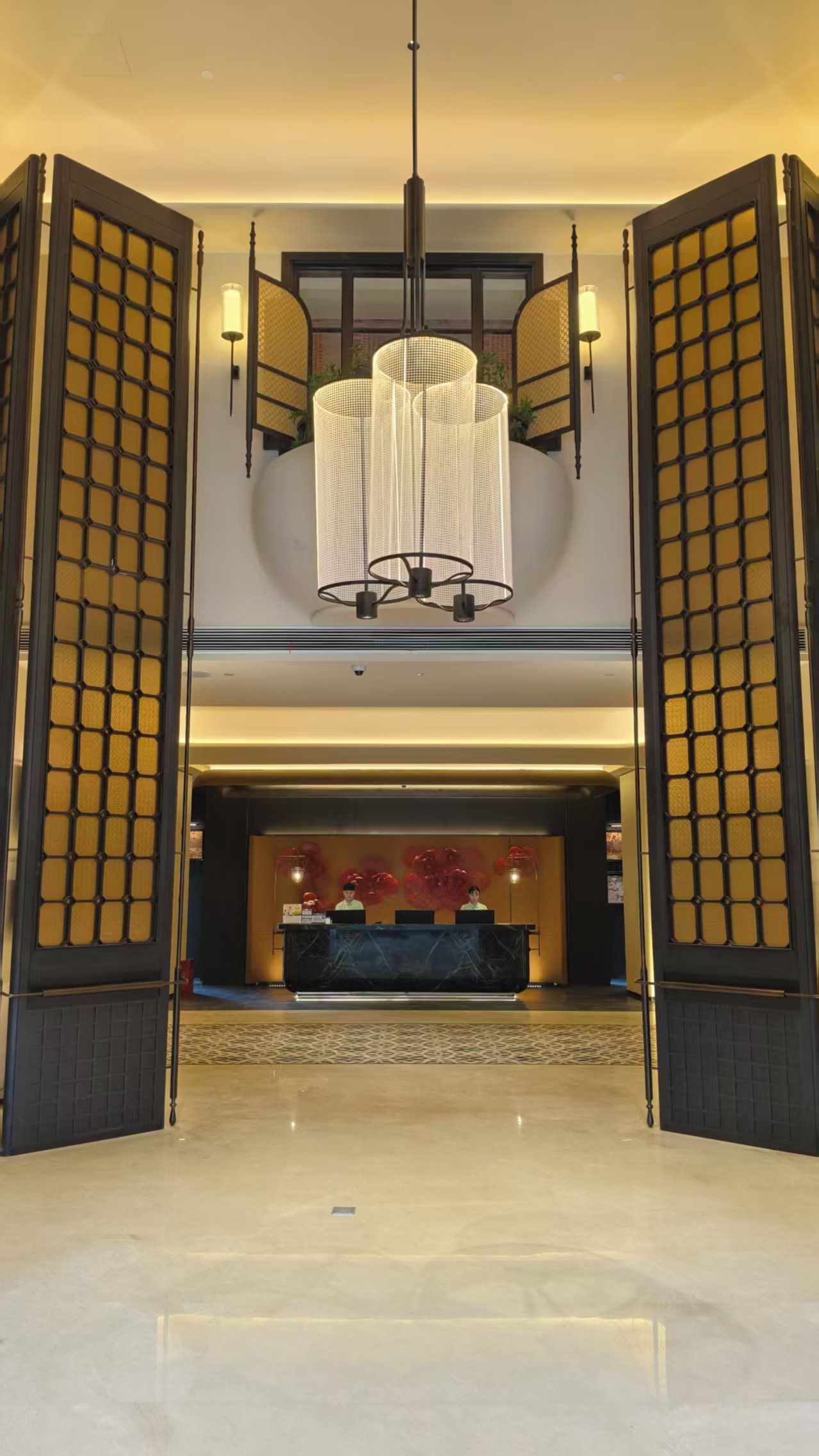 A hotel lobby with a reception desk, a large chandelier, and traditional Asian-style gates.