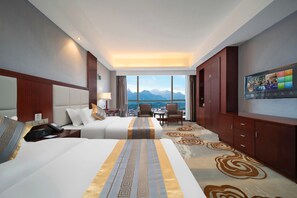 A hotel room with two beds, a TV, a desk, and a view of mountains. - Chensheng International Hotel (Zhangjiajie)