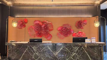 Un mostrador de recepción con encimera de mármol, dos portátiles y una pared con arte floral abstracto en rojo.