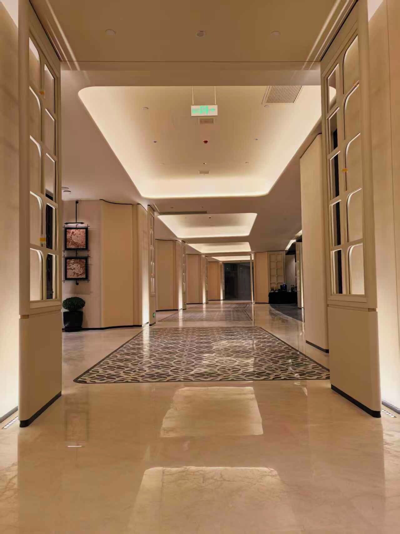 Un pasillo de hotel con alfombra estampada, iluminación empotrada y puertas espejadas.