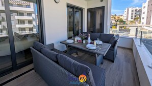 Un balcon avec une table à manger pour deux personnes, entouré de meubles en osier foncé.