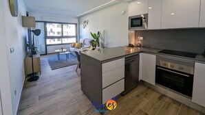 Une cuisine moderne avec des meubles blancs, un four à micro-ondes et un four traditionnel. On y trouve un coin repas avec une table et des chaises, ainsi qu’une grande fenêtre qui laisse entrer la lumière naturelle.