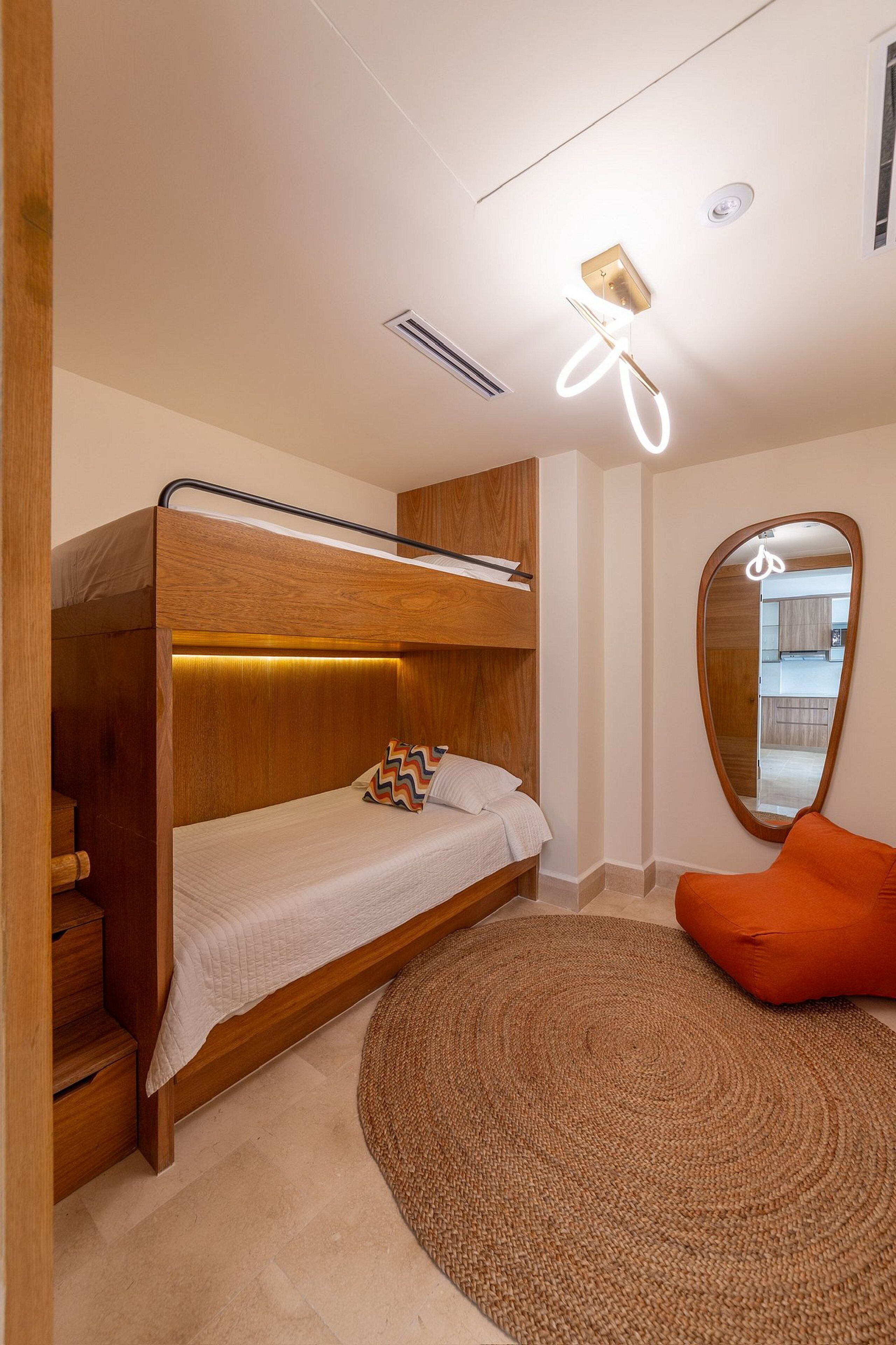 Una cama individual con cabecera de madera, un tapete redondo tejido y una luminaria de techo brillante.