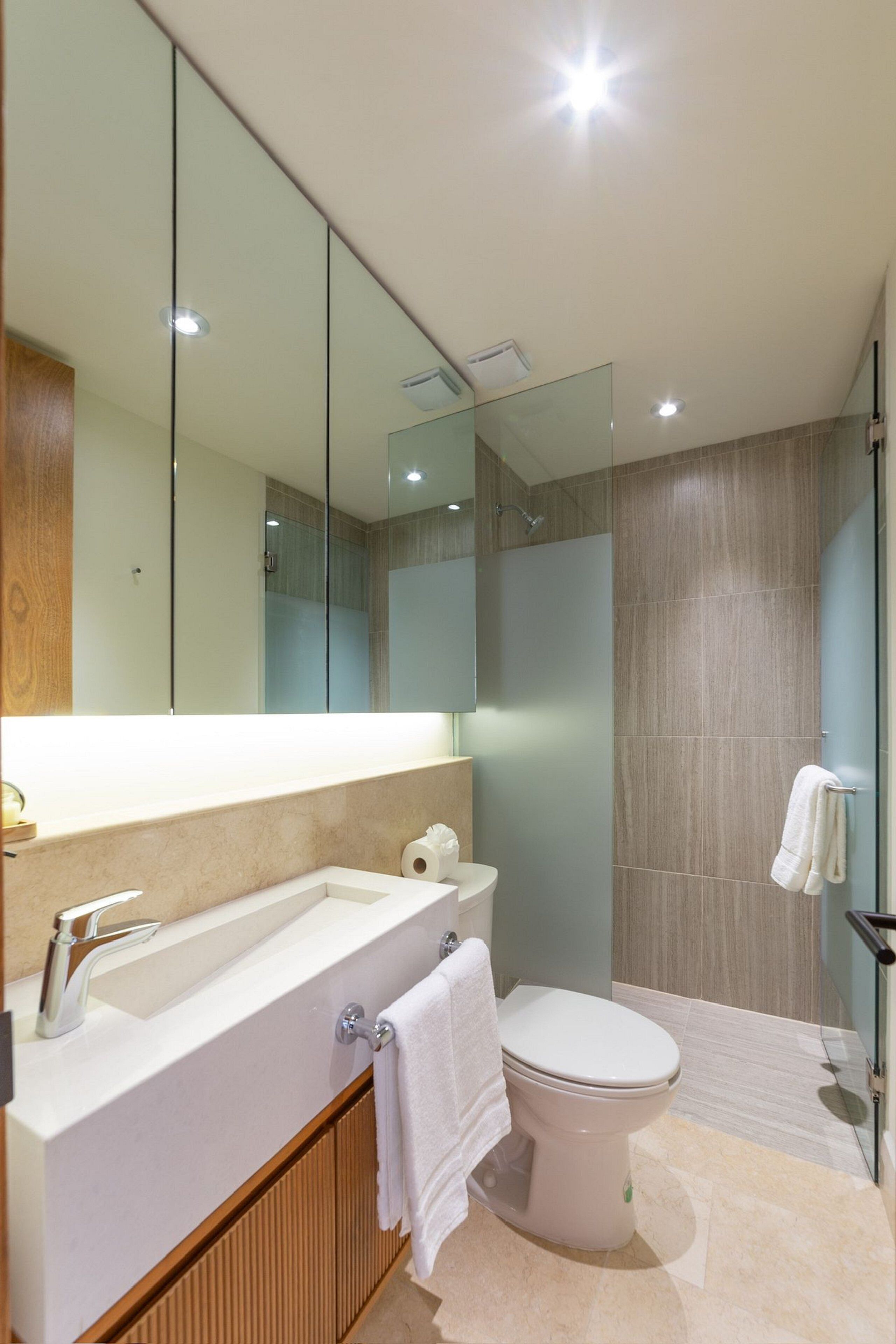 A modern bathroom with a large mirror, a white sink, a toilet, and a shower area.