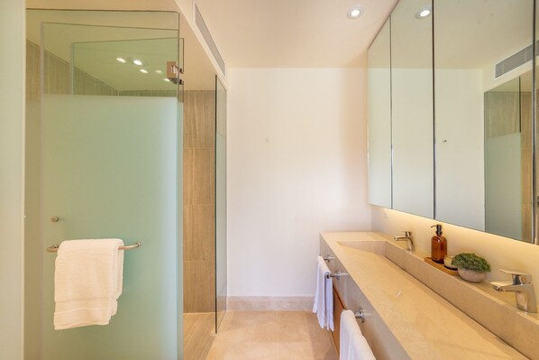 Un baño moderno con cabina de ducha de vidrio, un espejo grande y encimera color beige con un lavamanos y una planta pequeña.